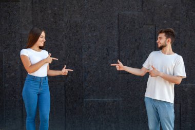 İfade, jest, duygular ve insan konsepti - Mutlu beyaz erkek ve kadın fotokopi alanının merkezini işaret ediyor, ona bakıyor ve siyah bir arka planda beyaz tişörtler içinde duruyor 