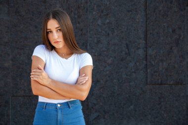 İfade, jest ve insan konsepti - üzgün beyaz bir kadın kollarını kavuşturup kameraya bakıyor, beyaz bir tişört ve kot pantolonla dışarıda duruyor fotokopi çekilen siyah bir arka planda 