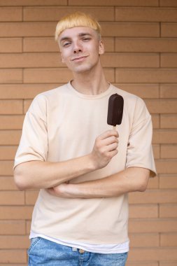 Yaz, tatlılar ve insanlar konsepti - bej tişört giymiş gülümseyen beyaz bir adam ve kolları dışarıda açık tuğla bir duvarın arkasında çaprazlanmış bir çubukta dondurma tutuyor. 