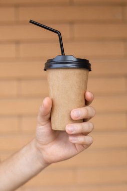 İçkiler, yaşam tarzı, tüketim ve insan konsepti - Beyaz erkek elleri, arka planda siyah kapaklı bir kahve fincanı ve fotokopi alanı olan tuğla bir duvarın üzerinde saman tutuyor