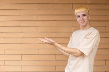 Jest, duygu, ifade ve insan konsepti - bej tişört ve kot giyen gülümseyen beyaz adam ellerini sol tarafta, dışarıda, tuğla bir duvarın arkasında fotokopi çekerken görülüyor
