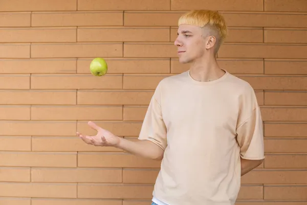 有機食品 健康的な食事と人々の概念 ヨーロッパのブロンドの男は側に緑のリンゴを投げ レンガの壁の背景にそれを見て 彼の手でそれをキャッチ — ストック写真