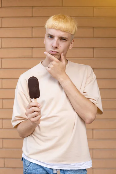 垃圾食品 糖果和人的概念 一个身穿米色T恤 头戴巧克力冰淇淋 头戴砖墙背景 用棍子盯着摄像机的正在沉思的白人男子 — 图库照片