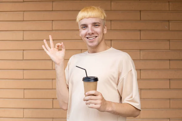 生活方式 姿势和人的观念 滑稽的白人男子穿着米色T恤 手举着手 在有复制空间的砖墙上端着一杯咖啡 — 图库照片