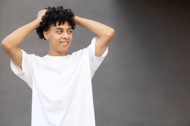 Jest, duygu, ifade ve insan konsepti - esrarengiz Amerikalı erkek kendini saçından tutuyor, beyaz tişört giyiyor, koyu gri arka planda fotokopi alanına bakıyor. 
