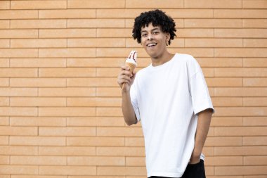 Yaşam tarzı, tatlı, tatlı ve insanlar konsepti - Burnunda beyaz dondurma ile tatmin olmuş, kameraya bakıyor ve tuğla duvar arkasında beyaz bir tişört giyiyor