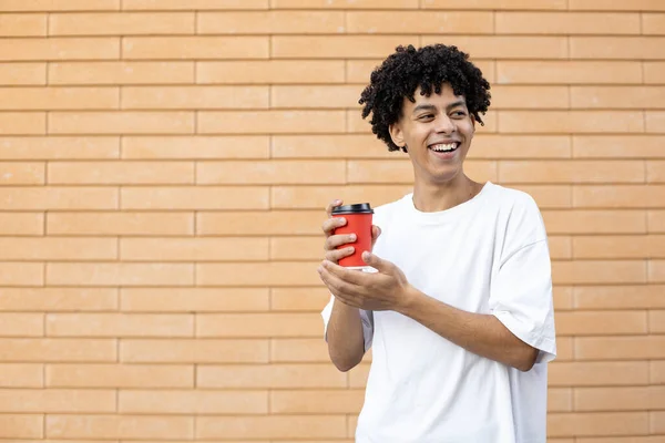 生活方式 消费和人的观念 笑着一头卷曲的非洲裔美国人 手里拿着一杯红咖啡 穿着一件白色T恤 看着砖墙的背景 — 图库照片