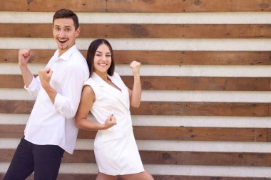 Beyaz elbiseli tatmin olmuş Avrupalı erkek ve kadın başarıyı kutluyor ve kahverengi bir arka planda birbirlerine sırtlarını dönerek fotokopi çekiyorlar.