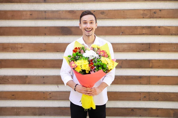 鲜花与幸福的概念 穿着白衬衫 笑容满面的英俊男子 手持一大束花 背景是褐色的 背带着复制的空间 — 图库照片