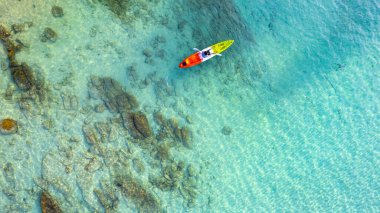 Mavi denizdeki bir kanonun havadan görünüşü. Kano yapan bir kadın. Su sporları aktiviteleri yapıyor..
