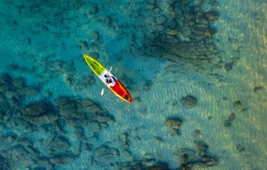Mavi denizdeki bir kanonun havadan görünüşü. Kano yapan bir kadın. Su sporları aktiviteleri yapıyor..