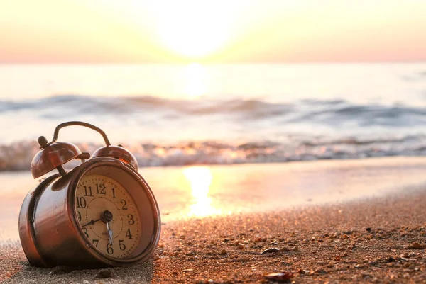 Yeni bir günün sabahı, kumsalın güneş ışığında çalar saat. Sağlık kavramı.