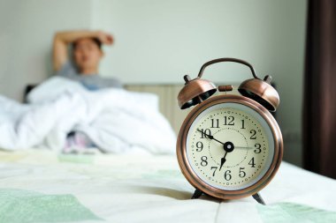 Çalar saat. Mutsuz genç adamın başı ağrıyor. Uyku uykusuzluğu gece yatağında sağlık hizmetleri konseptinde..