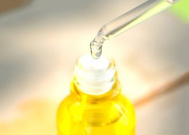 Yüzün serum kolajen nemlendiricisini açık sarı şişe yumuşak ışık arka planına döküyorum. Koruyucu cilt bakımı yüz özü yağı, C vitamini güzellik ve kaplıca konsepti..