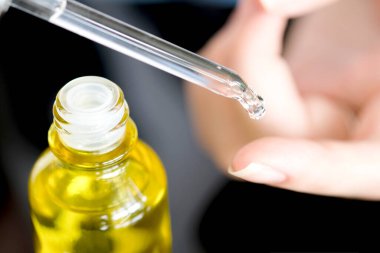 Yüzün serum kolajen nemlendiricisini açık sarı şişe yumuşak ışık arka planına döküyorum. Koruyucu cilt bakımı yüz özü yağı, C vitamini güzellik ve kaplıca konsepti..