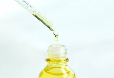 Yüzün serum kolajen nemlendiricisini açık sarı şişe yumuşak ışık arka planına döküyorum. Koruyucu cilt bakımı yüz özü yağı, C vitamini güzellik ve kaplıca konsepti..