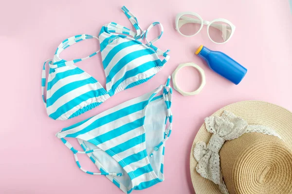 Yaz aksesuarları ve mavi yüzme bikini, güneş gözlüğü ve plajda seyahat için şapka giyerler. Pembe renkli arka plan. Moda ve turizm konsepti