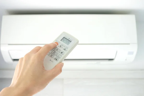 リモコンを使って人の手を開くエアコンは寝室で25度まで冷やされています 健康の概念と省エネルギー — ストック写真