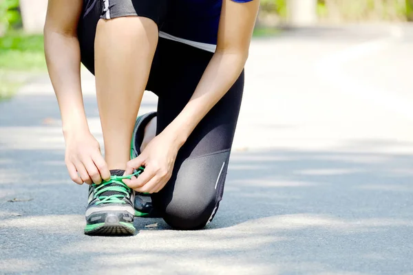 公園内の道路をジョギングするためのランニングシューズレースを結ぶ女性 — ストック写真