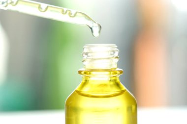 Yüzün serum kolajen nemlendiricisini açık sarı şişe yumuşak ışık arka planına döküyorum. Koruyucu cilt bakımı yüz özü yağı, C vitamini güzellik ve kaplıca konsepti..
