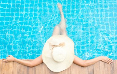 Vücut güzelliği olan bir kadın, hafta sonları lüks bir tatil köyünde havuz başında havuz bacakları ve ayakları üzerinde dinlenen büyük bir şapka giyer. Güzellik ve tatil kavramını benimser.