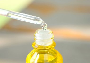 Yüzün serum kolajen nemlendiricisini açık sarı şişe yumuşak ışık arka planına döküyorum. Koruyucu cilt bakımı yüz özü yağı, C vitamini güzellik ve kaplıca konsepti..