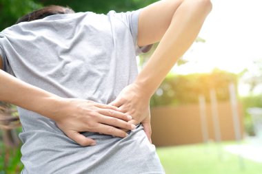 Kadının eli belinden sıkıştı ve sırtı parkta acı içinde kıvranıyor. Egzersiz nedeni.