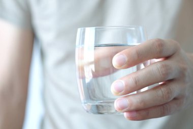 Sabah, bir adamın eli içmek için temiz bir bardak su tutuyor..