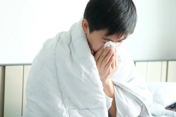 Sick man is flu, using a paper napkin and he have a runny nose. And he was covered in warm cloth.Health concept