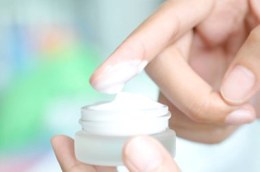 Güzel bir kadının elleri, yüzüne serum kolajen nemlendirici dökerek berrak sarı şişe yumuşak ışık arka planına döküyor. Koruyucu cilt bakımı yüz özü yağı, C vitamini güzellik ve kaplıca.