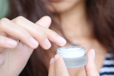 Güzel bir kadının elleri, yüzüne serum kolajen nemlendirici dökerek berrak sarı şişe yumuşak ışık arka planına döküyor. Koruyucu cilt bakımı yüz özü yağı, C vitamini güzellik ve kaplıca.