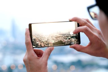 Gençler şehirdeki binaların fotoğraflarını çekiyor. Gün doğumu zamanı. Yüksek açılı bir fotoğraf telefonu kullanıyor. Seyahat kavramları ve teknoloji.