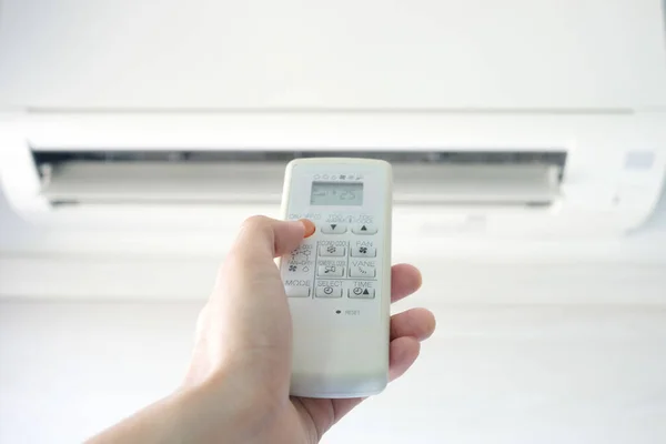リモコンを使って人の手を開くエアコンは寝室で25度まで冷やされています 健康の概念と省エネルギー — ストック写真