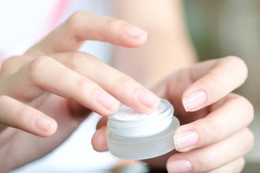 Güzel bir kadının elleri, yüzüne serum kolajen nemlendirici dökerek berrak sarı şişe yumuşak ışık arka planına döküyor. Koruyucu cilt bakımı yüz özü yağı, C vitamini güzellik ve kaplıca.