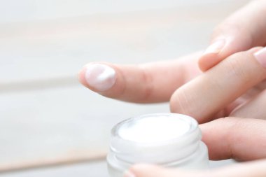 Güzel bir kadının elleri, yüzüne serum kolajen nemlendirici dökerek berrak sarı şişe yumuşak ışık arka planına döküyor. Koruyucu cilt bakımı yüz özü yağı, C vitamini güzellik ve kaplıca.