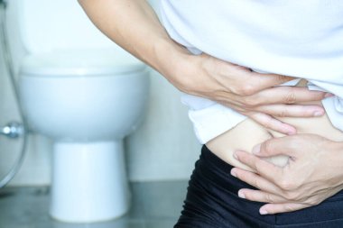 The concept of constipation. The man's hand is holding toilet paper. Stained Toilet bathroom background.