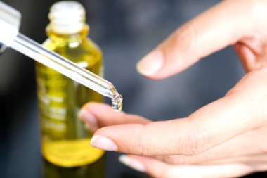 Güzel bir kadının elleri, yüzüne serum kolajen nemlendirici dökerek berrak sarı şişe yumuşak ışık arka planına döküyor. Koruyucu cilt bakımı yüz özü yağı, C vitamini güzellik ve kaplıca.