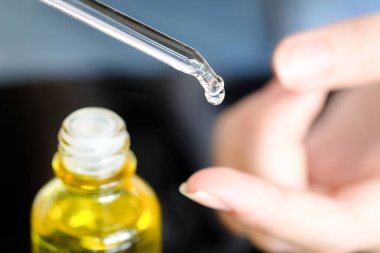 Güzel bir kadının elleri, yüzüne serum kolajen nemlendirici dökerek berrak sarı şişe yumuşak ışık arka planına döküyor. Koruyucu cilt bakımı yüz özü yağı, C vitamini güzellik ve kaplıca.