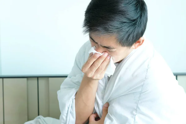 Sick man is flu, using a paper napkin and he have a runny nose. And he was covered in warm cloth.Health concept