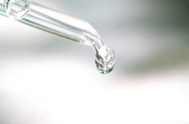 Güzel bir kadının elleri, yüzüne serum kolajen nemlendirici dökerek berrak sarı şişe yumuşak ışık arka planına döküyor. Koruyucu cilt bakımı yüz özü yağı, C vitamini güzellik ve kaplıca.