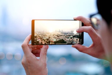 Gençler şehirdeki binaların fotoğraflarını çekiyor. Gün doğumu zamanı. Yüksek açılı bir fotoğraf telefonu kullanıyor. Seyahat kavramları ve teknoloji.