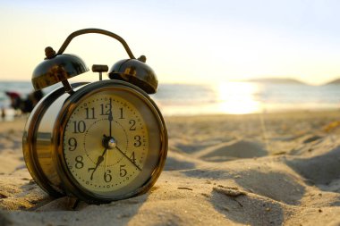Yeni bir günün sabahı, kumsalın güneş ışığında çalar saat. Sağlık ve tatil kavramı.