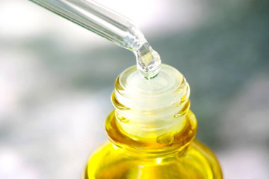 Güzel bir kadının elleri, yüzüne serum kolajen nemlendirici dökerek berrak sarı şişe yumuşak ışık arka planına döküyor. Koruyucu cilt bakımı yüz özü yağı, C vitamini güzellik ve kaplıca.