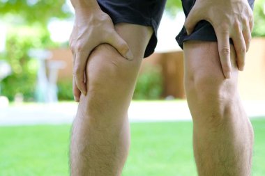 Diz ağrısı. Adam yatakta oturuyor. Eli dizinden sıkıştı. Acıyı dindirmek için ayaklarının ağrıması ve kaslarının yorulması. sağlık kavramları.