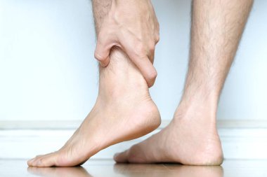 Bir erkek bacağının resmi ve adamın eli ayak bileğinde ağrı var.