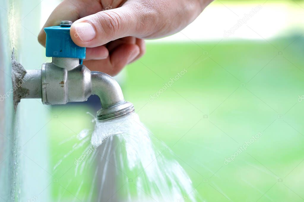 Woman's hand, she opened the faucet, watering the trees, blurred background, natural green.