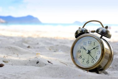Yeni bir günün sabahı, kumsalın güneş ışığında çalar saat. Sağlık ve tatil kavramı.