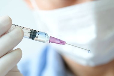 Doktorun elinde hastanede bir şırınga ve mavi bir aşı şişesi var. Sağlık ve tıbbi kavramlar