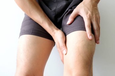 Diz ağrısı. Adam yatakta oturuyor. Eli dizinden sıkıştı. Acıyı dindirmek için ayaklarının ağrıması ve kaslarının yorulması. sağlık kavramları.