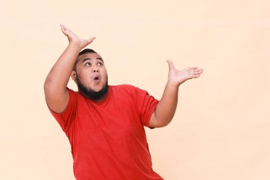 Genç Asyalı adam şaşırmış ve haykırıyor elleri kırmızı arka planda izole bir şekilde sağa dönük..